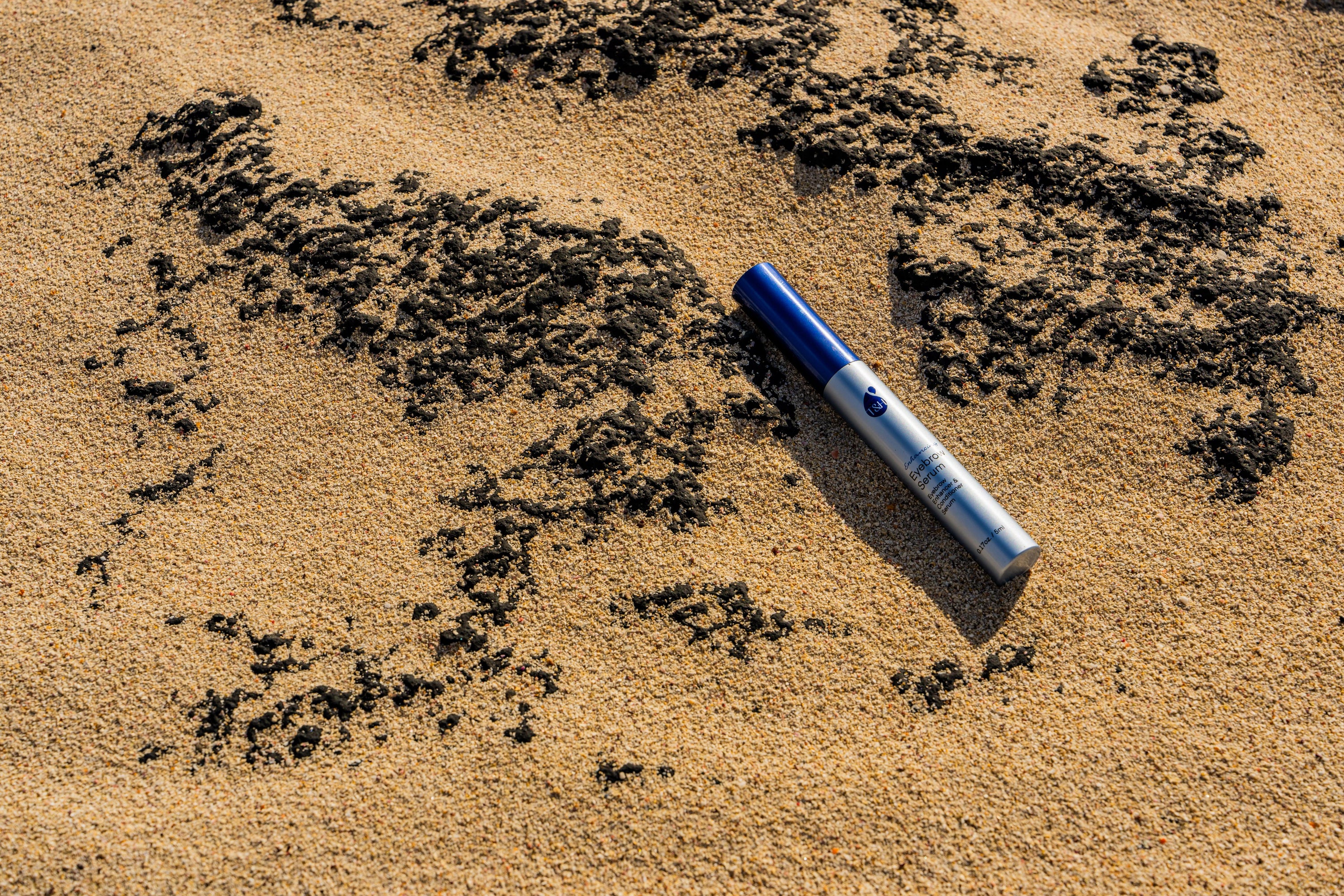 bottle of eyebrow serum on sand