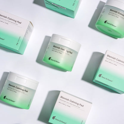 Multiple jars and boxes of Terez &amp; Honor Blemish Calming Pads arranged in an aesthetically pleasing pattern on a bright background, emphasizing the clean, clinical design of the skincare product packaging.