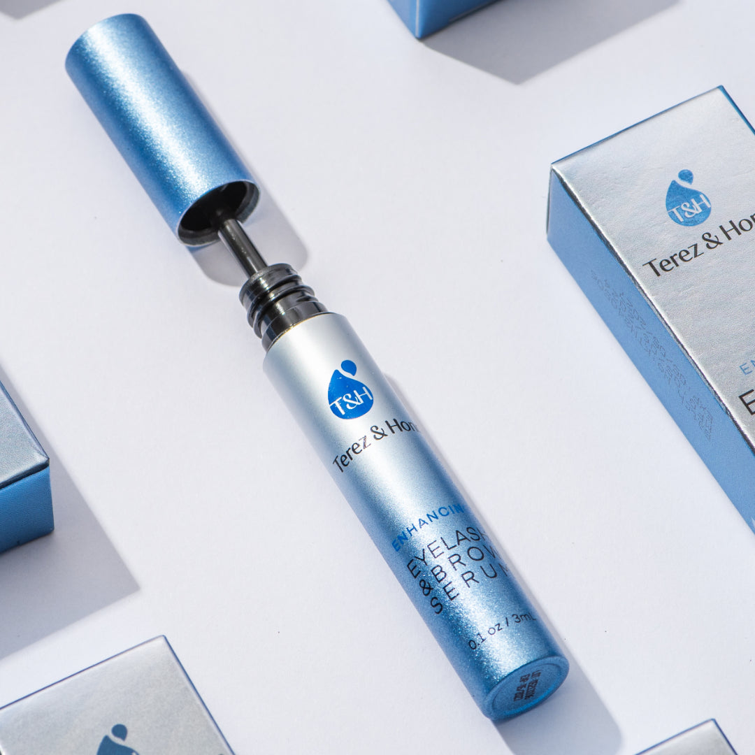 Terez & Honor Eyelash and Brow Serum displayed with its metallic blue packaging and opened applicator wand, set against a clean white background with additional product boxes in view