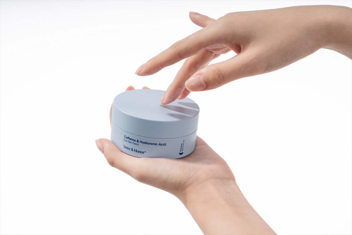 Hands holding a jar of Terez & Honor Caffeine & Hyaluronic Acid Eye Gel Patch, with fingers gently touching the lid of the jar